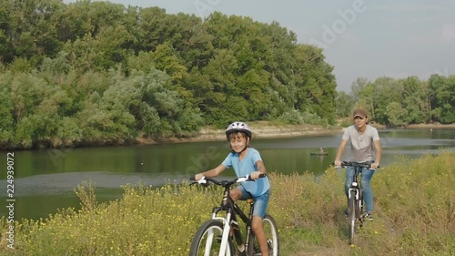 Family on bikes. A child with mother cycling in nature. A woman with a child on bicycles ride along the river. photo