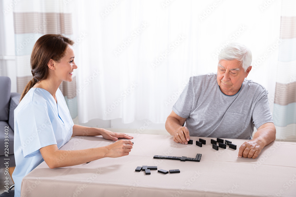 Obraz premium Caretaker Looking At Elder Man Playing Dominoes