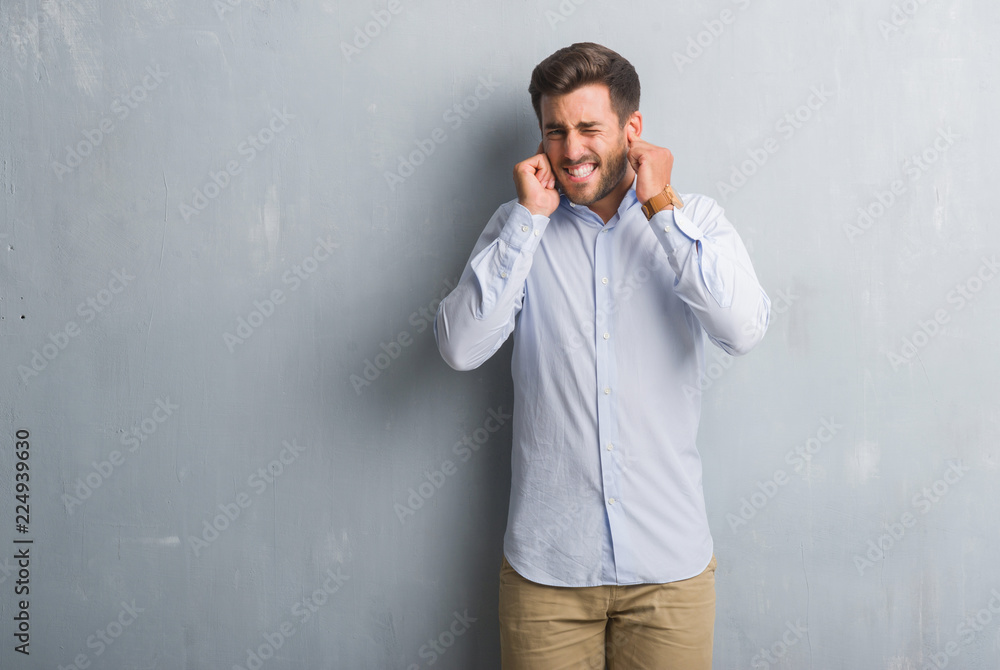 Handsome young business man over grey grunge wall wearing elegant shirt covering ears with fingers with annoyed expression for the noise of loud music. Deaf concept. Handsome young business man over grey grunge wall wearing elegant shirt covering ears with fingers with annoyed expression for the noise of loud music. Deaf concept.