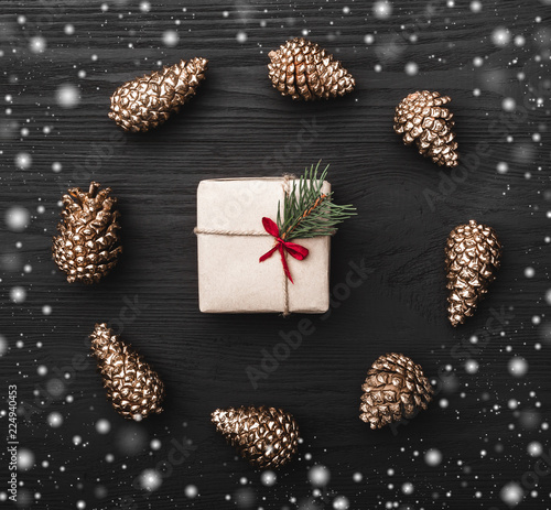 Circle from golden fir pines and gift, present box in center, on black, dark wooden background in snow, creating a xmas greeting card