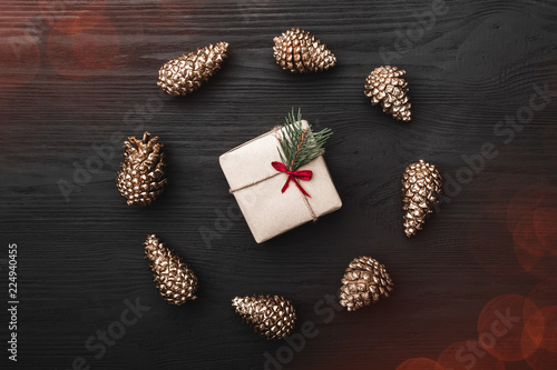 Circle from golden fir pines and gift, present box in center, on black, dark wooden background, creating a xmas greeting card