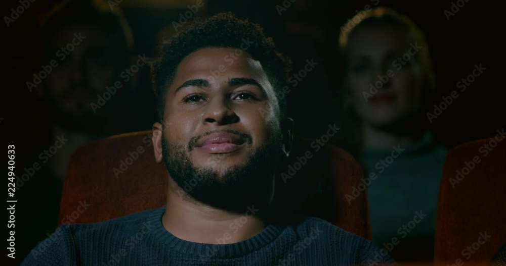 A young man siting in a movie theatre smiling, enjoying watching a movie A young man siting in a movie theatre smiling, enjoying watching a movie