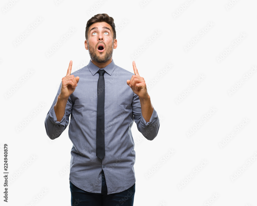 Young handsome business man over isolated background amazed and surprised looking up and pointing with fingers and raised arms. Young handsome business man over isolated background amazed and surprised looking up and pointing with fingers and raised arms.