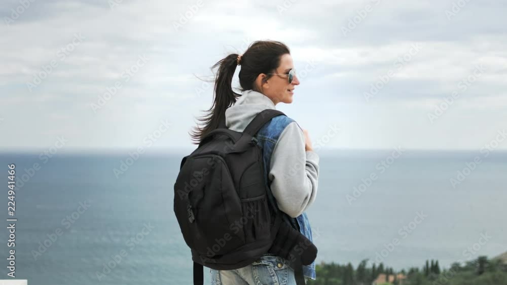Hiker woman in sunglasses with backpack admiring amazing seascape at rainy overcast weather Hiker woman in sunglasses with backpack admiring amazing seascape at rainy overcast weather
