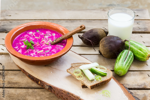 Traditional lithuanian vegetable soup made of beetroot (beet), cucumber, dill, green onion and sour cream (kefir) on the wood backgound with ingredients