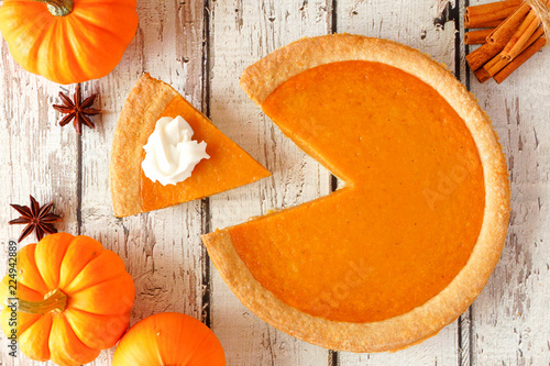 Pumpkin pie with slice removed.  Top view table scene on a rustic white wood background. photo