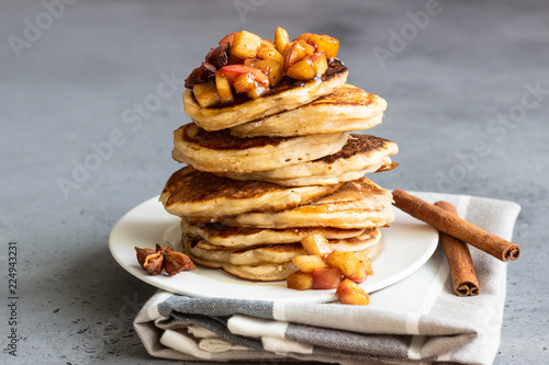 Stack of delicious sweet and spicy apple pancakes with fried caramelized apples, anise, cinnamon and honey on a white plate. Autumn breakfast. Copy space.