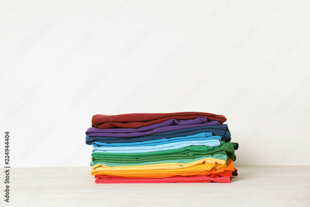 Stack of bright folded clothes on table against white background. Space for text Stack of bright folded clothes on table against white background. Space for text