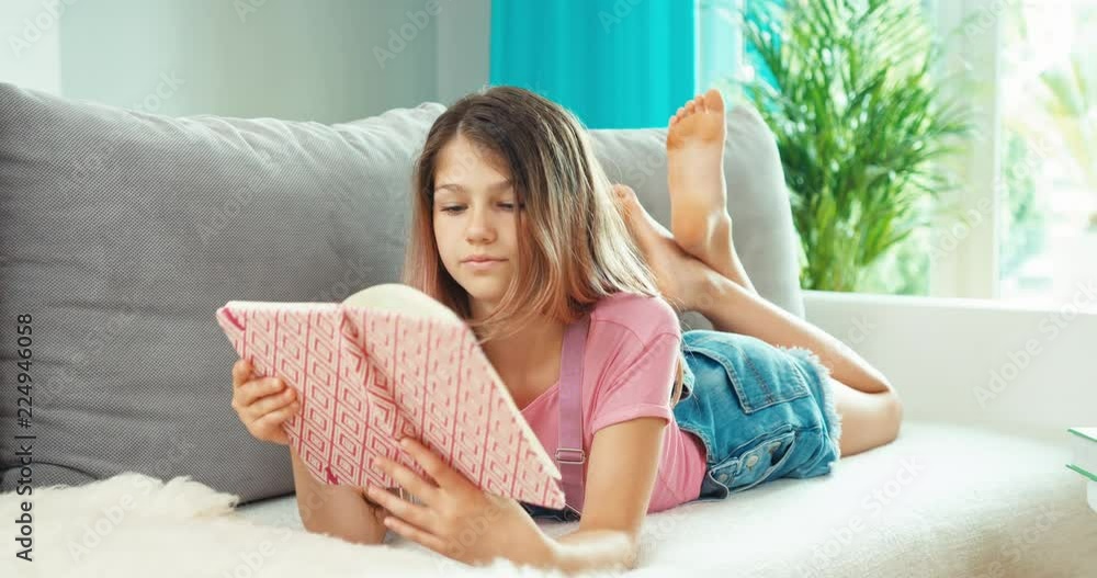 Teenage girl looking in her notebook, smiling, lying on the sofa Teenage girl looking in her notebook, smiling, lying on the sofa