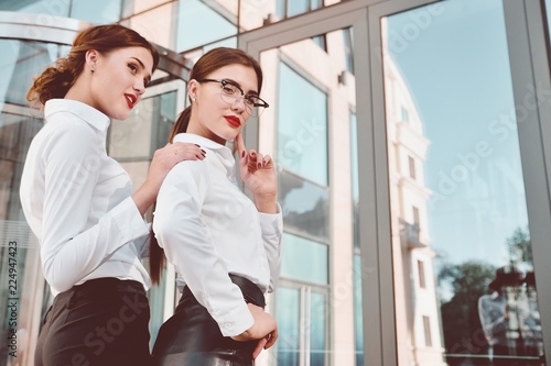Two girls in white shirts on the background of a glass office building with bright red lipstick on their lips