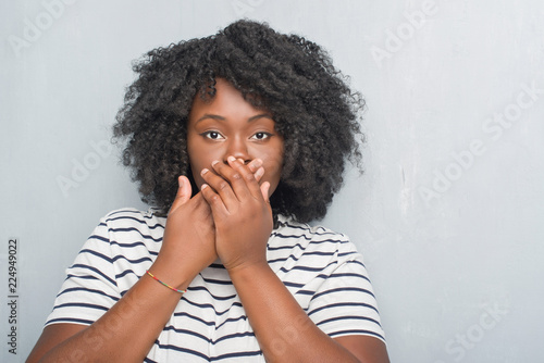 Young african american plus size woman over grey grunge wall shocked covering mouth with hands for mistake. Secret concept.