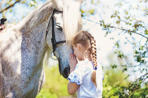 Cute little girl whith white horse in blooming apple orchard