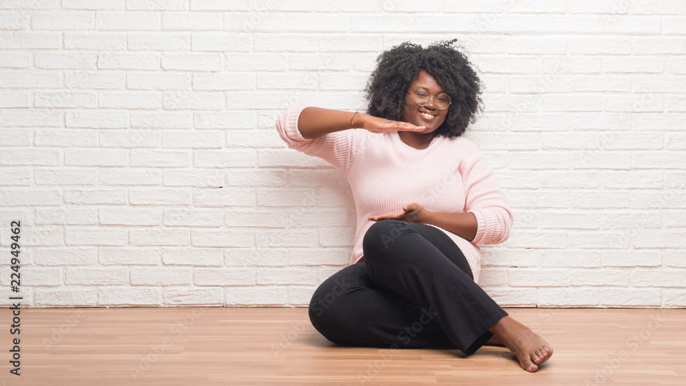 Young african american woman sitting on the floor at home gesturing with hands showing big and large size sign, measure symbol. Smiling looking at the camera. Measuring concept. Young african american woman sitting on the floor at home gesturing with hands showing big and large size sign, measure symbol. Smiling looking at the camera. Measuring concept.
