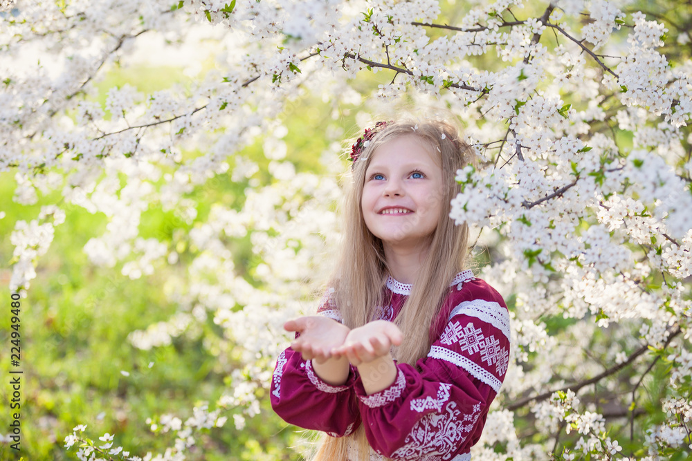 Lovely lttle girl stands under a blooming plum in park in ethnic ukrainian dress Lovely lttle girl stands under a blooming plum in park in ethnic ukrainian dress