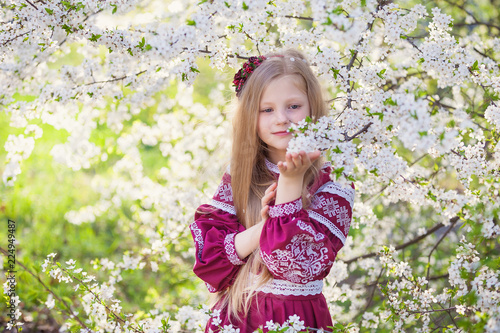 Lovely lttle girl stands under a blooming plum in park in ethnic ukrainian dress