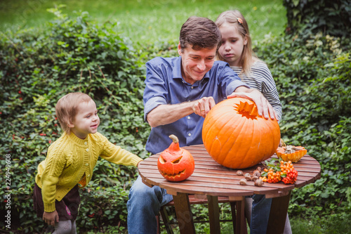 Happy halloween. Father and two daughter carving pumpkin for Halloween outside. Happy family photo
