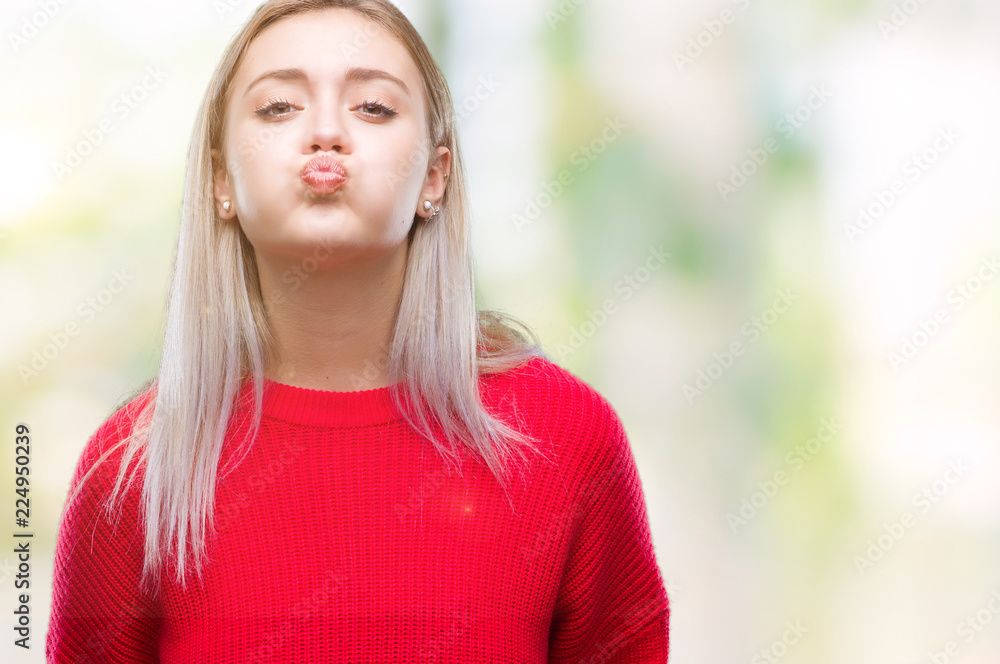 Young blonde woman wearing winter sweater over isolated background puffing cheeks with funny face. Mouth inflated with air, crazy expression.