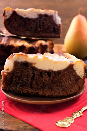 Cut pieces of chocolate dough pie with a curd layer, ripe pear on a red napkin.