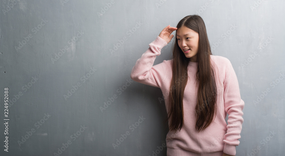 Young Chinese woman over grey wall very happy and smiling looking far away with hand over head. Searching concept. Young Chinese woman over grey wall very happy and smiling looking far away with hand over head. Searching concept.