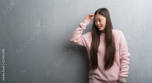Young Chinese woman over grey wall very happy and smiling looking far away with hand over head. Searching concept.
