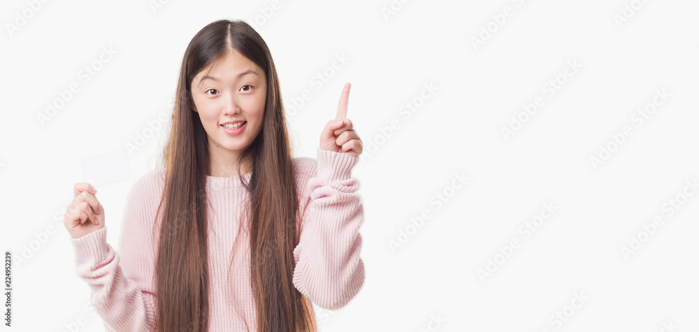 Young Chinese woman over isolated background holding visit card surprised with an idea or question pointing finger with happy face, number one Young Chinese woman over isolated background holding visit card surprised with an idea or question pointing finger with happy face, number one