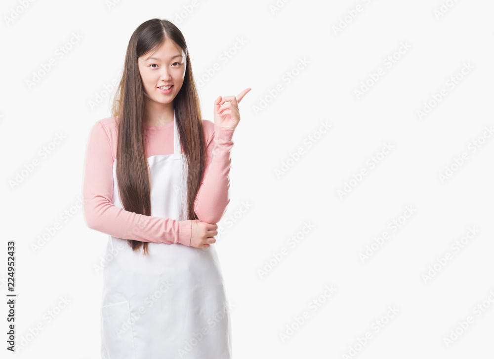 Young Chinese shop owner woman over isolated background wearing white apron very happy pointing with hand and finger to the side Young Chinese shop owner woman over isolated background wearing white apron very happy pointing with hand and finger to the side