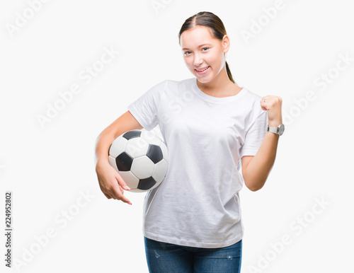 Young beautiful caucasian woman holding soccer football ball over isolated background screaming proud and celebrating victory and success very excited, cheering emotion © Krakenimages.com