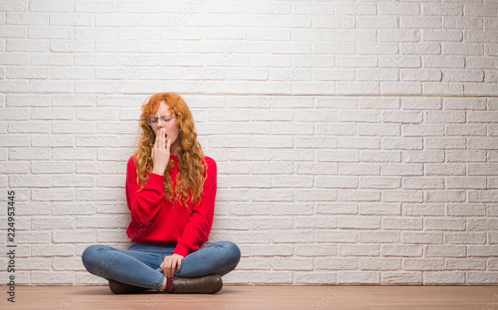 Young redhead woman sitting over brick wall bored yawning tired covering mouth with hand. Restless and sleepiness. Young redhead woman sitting over brick wall bored yawning tired covering mouth with hand. Restless and sleepiness.