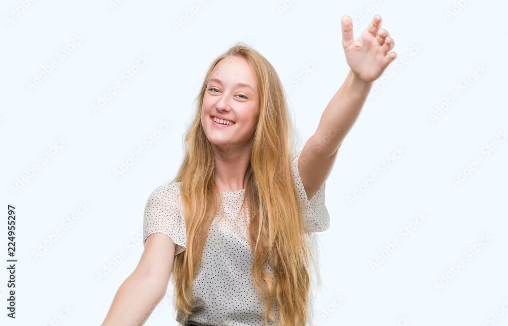 Blonde teenager woman wearing moles shirt looking at the camera smiling with open arms for hug. Cheerful expression embracing happiness. Blonde teenager woman wearing moles shirt looking at the camera smiling with open arms for hug. Cheerful expression embracing happiness.