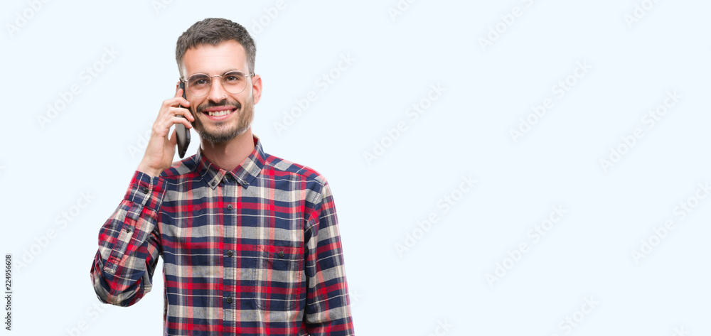 Young hipster adult man talking on the phone with a happy face standing and smiling with a confident smile showing teeth Young hipster adult man talking on the phone with a happy face standing and smiling with a confident smile showing teeth