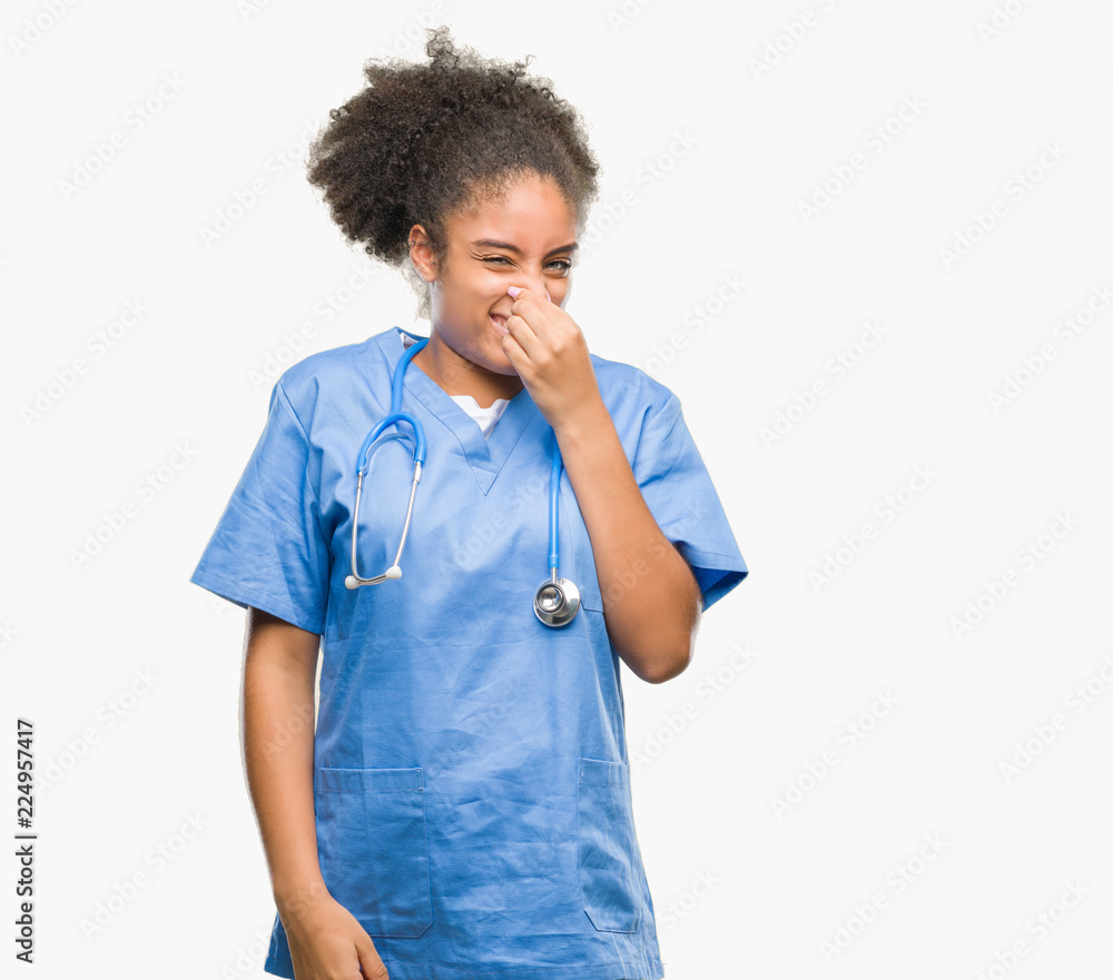 Young afro american doctor woman over isolated background smelling something stinky and disgusting, intolerable smell, holding breath with fingers on nose. Bad smells concept. Young afro american doctor woman over isolated background smelling something stinky and disgusting, intolerable smell, holding breath with fingers on nose. Bad smells concept.