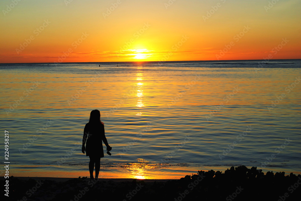 Fototapeta premium Silhouette of an unrecognizable woman watching the setting sun in Saipan, Northern Mariana Islands.