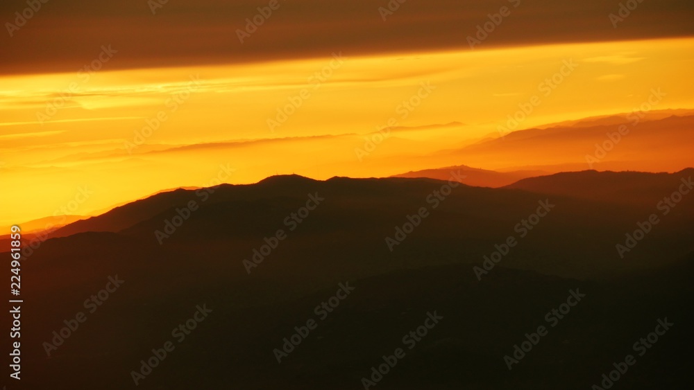 The sun rises above the mountaintops casting a golden orange glow in the skies