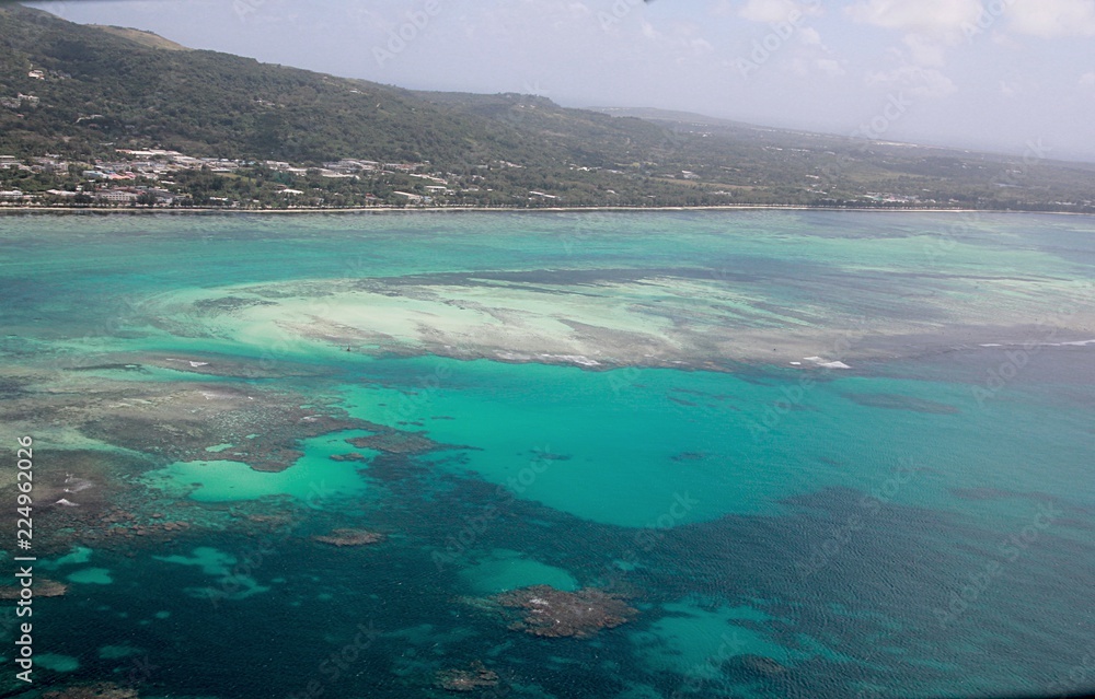 Saipan lagoon aerial view with its different shades of blue and green waters and the Beach Road in the distance