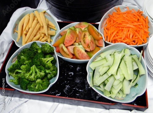 Colorful vegetables including young corn, cucumber, cauliflower, tomatoes and shredded carrots in separate white bowls