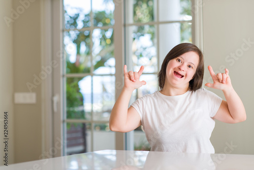 Down syndrome woman at home shouting with crazy expression doing rock symbol with hands up. Music star. Heavy concept.