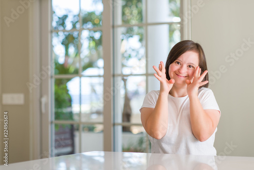 Down syndrome woman at home smiling crossing fingers with hope and eyes closed. Luck and superstitious concept. © Krakenimages.com