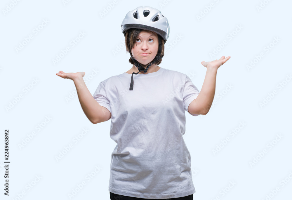 Young adult cyclist woman with down syndrome wearing safety helmet over isolated background clueless and confused expression with arms and hands raised. Doubt concept. Young adult cyclist woman with down syndrome wearing safety helmet over isolated background clueless and confused expression with arms and hands raised. Doubt concept.