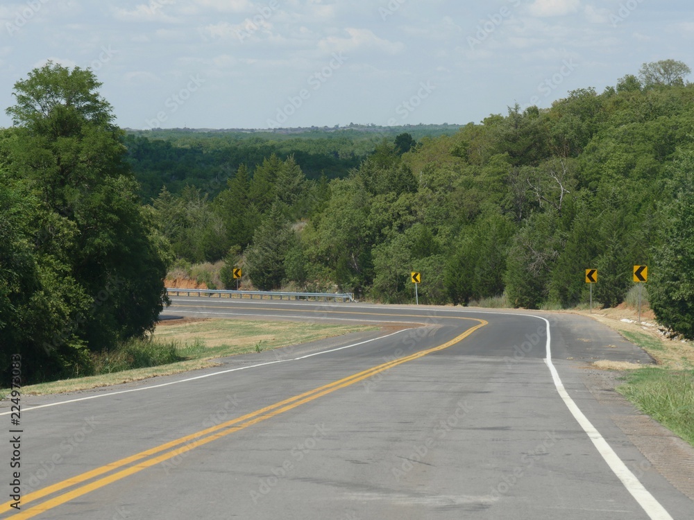 Scenic curved road with danger signs with green forests and foliage in the background Scenic curved road with danger signs with green forests and foliage in the background
