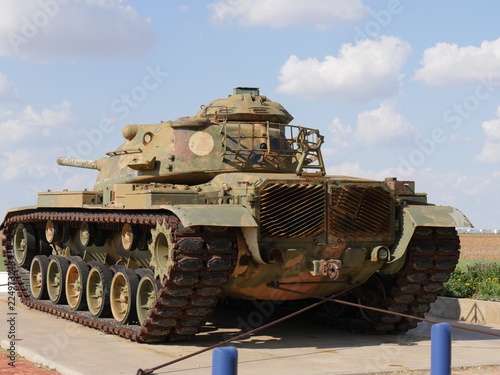 Close up shot of a military tank by the roadside with blue and white skies in the background