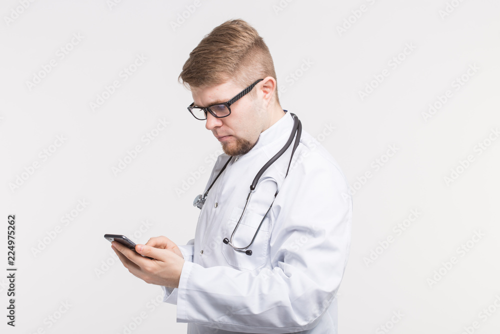 Health and medicine - doctor wearing the stethoscope, looking at phones screen on white background Health and medicine - doctor wearing the stethoscope, looking at phones screen on white background