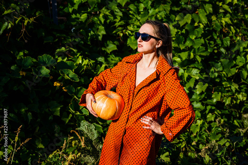 a young white woman in the orange coat on a background of green leaves