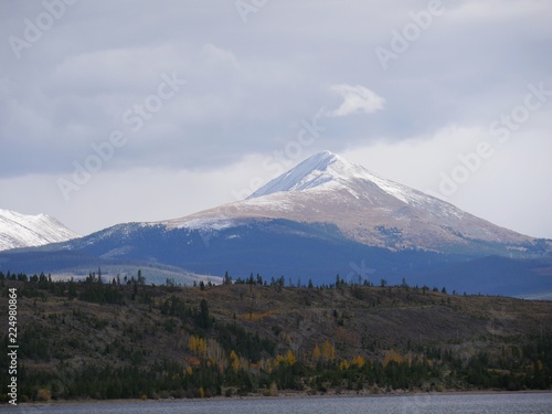 Snow-capped mountains tower above the jungles of Summit County  with Dillon Lake or Dillon Reservoir at the foot of the hills.