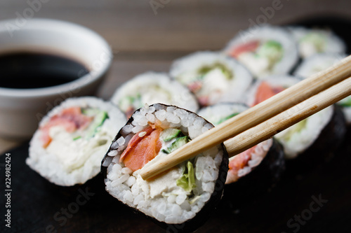 Eating sushi. Food photo, Japanese restaurant, dinner. Pair of chopsticks taking sushi roll from plate, close up