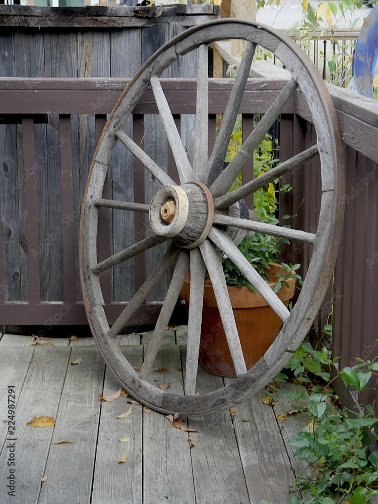 Old wooden wheel of a wagon leaning on a wooden balcony outdoors Old wooden wheel of a wagon leaning on a wooden balcony outdoors