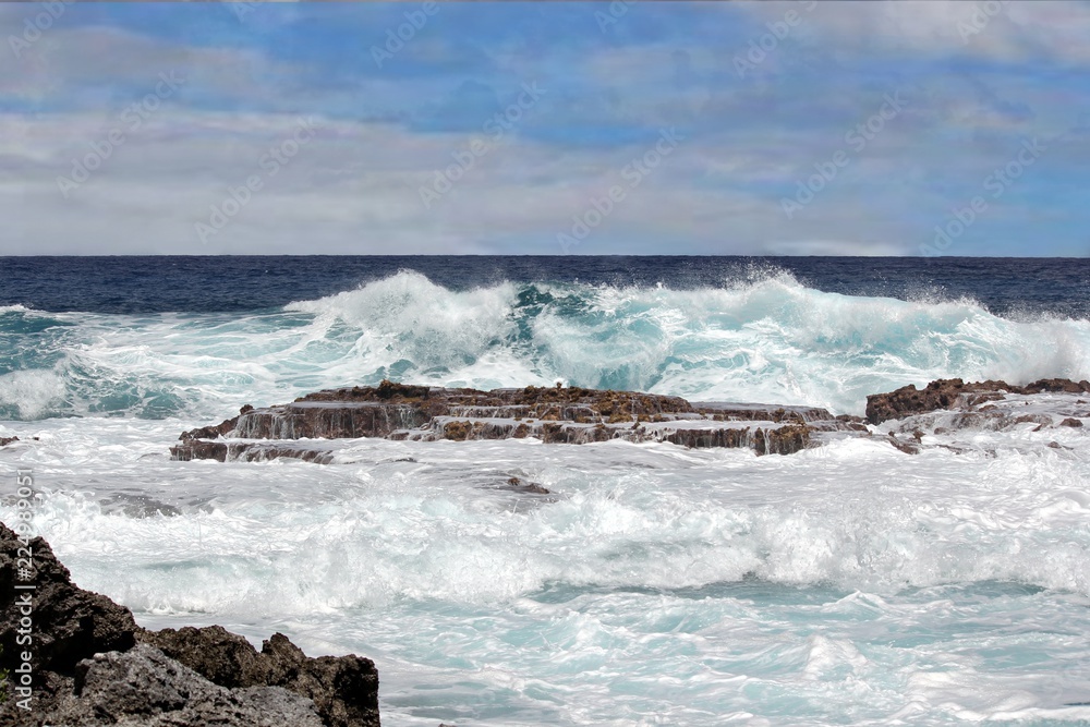 Angry waves rolling and breaking against the coral stone platforms and filling up the natural swimming hole during high tide at a tropical island 