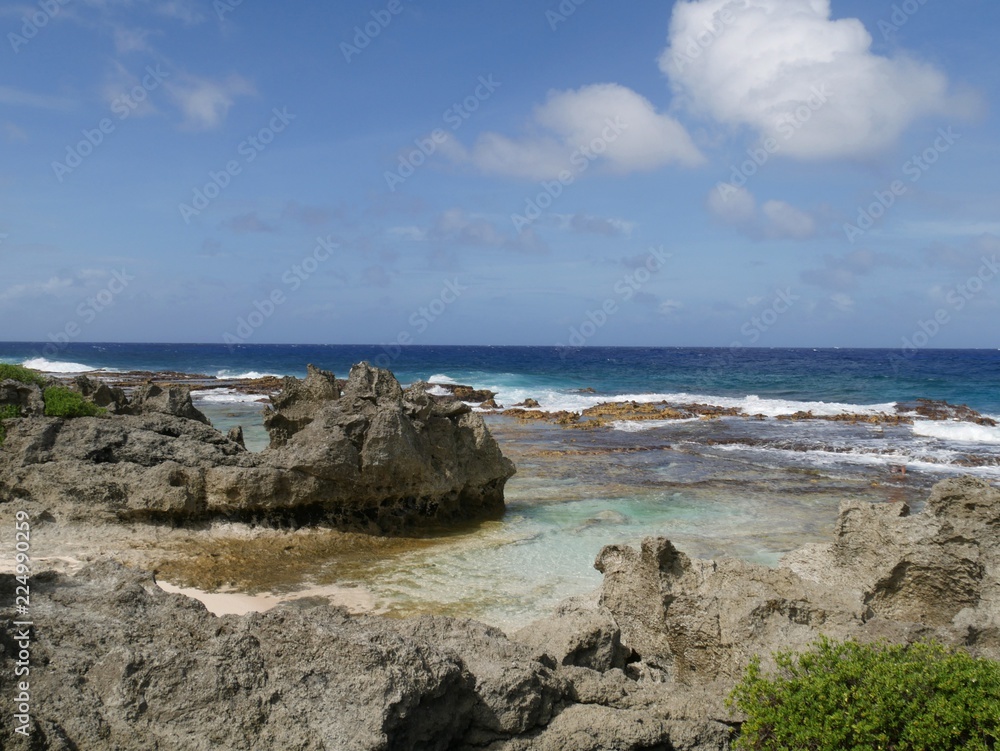 Scenic coastal view with rocks and corals bordering a beach in the tropical island of Rota, Northern Mariana Islands on a bright sunny day