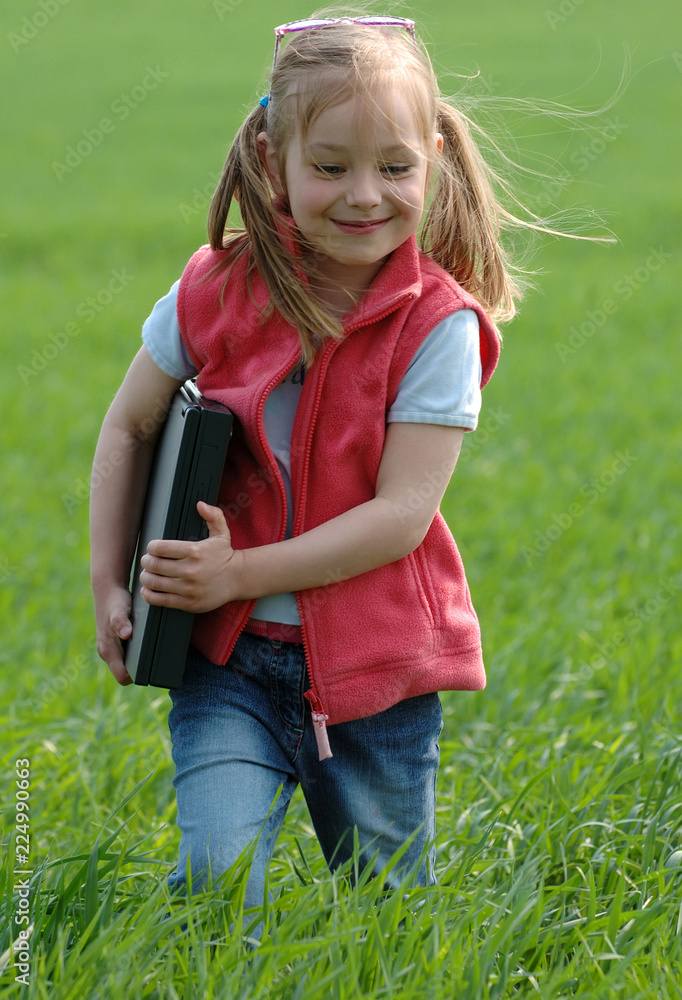 Fototapeta premium Little girl with a laptop on green field