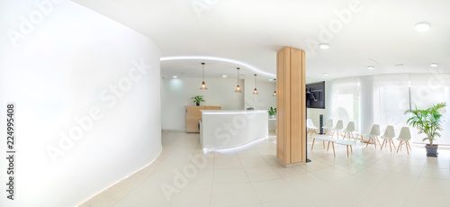 Vászonkép Panorama of a bright reception and waiting room in a clinic with desk, modern chairs and plants