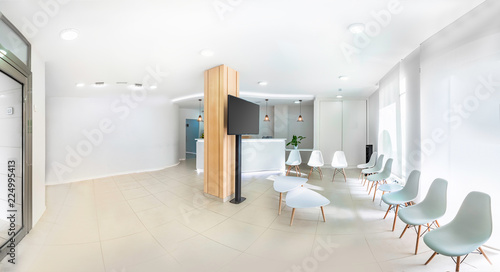 Panorama of a bright reception and waiting room in a clinic with desk, modern chairs and plants. Indoor mockup with screen with copy space. photo